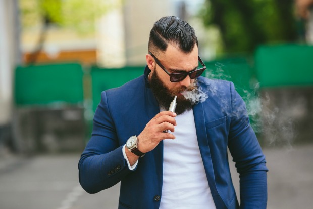 İyi giyimli sakallı bir adam elektronik sigara içerken.